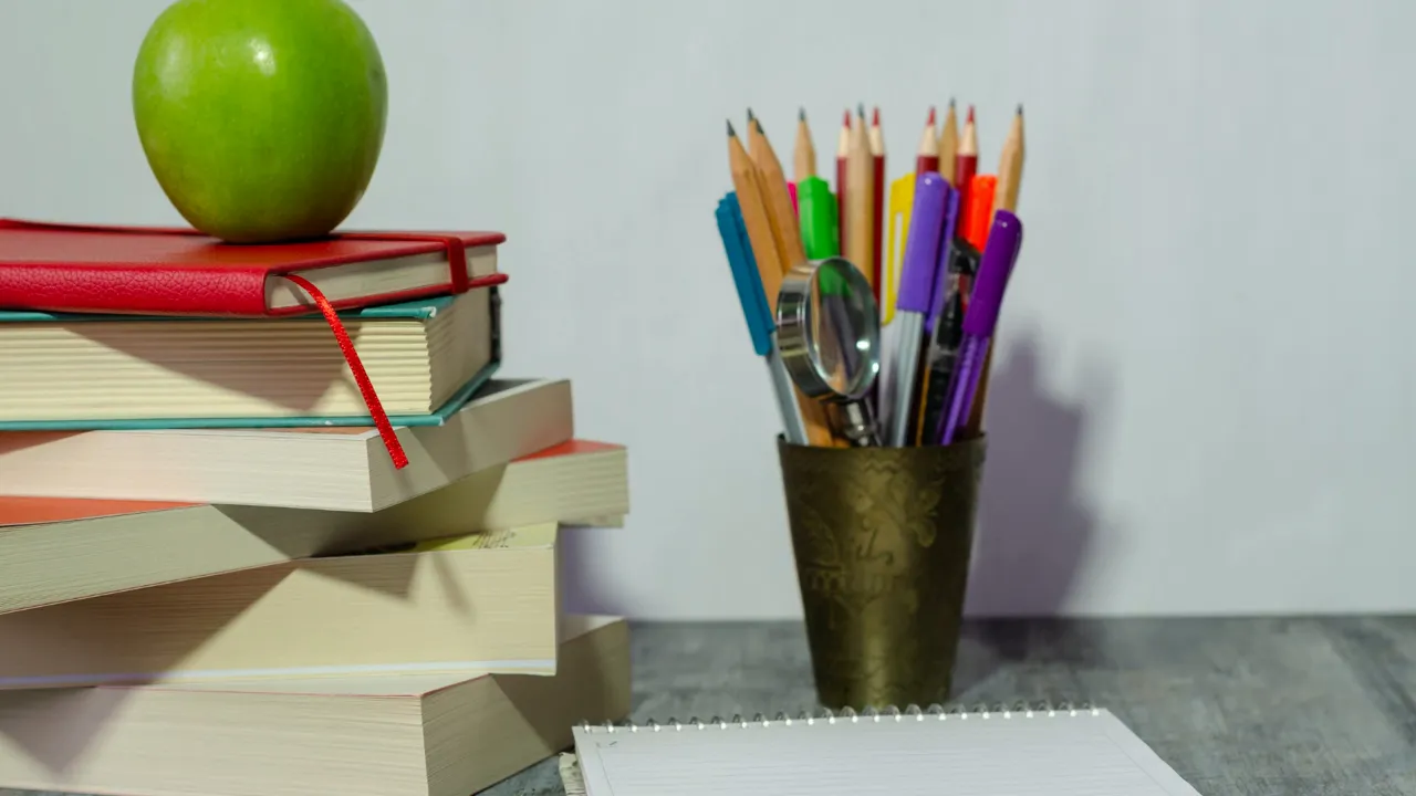 Stack of books with an apple, a cup of pencils and a notebook on a desk — classroom review supplies.