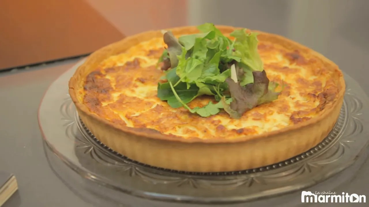 Quiche lorraine dorée sur un plat de service avec une salade verte au centre