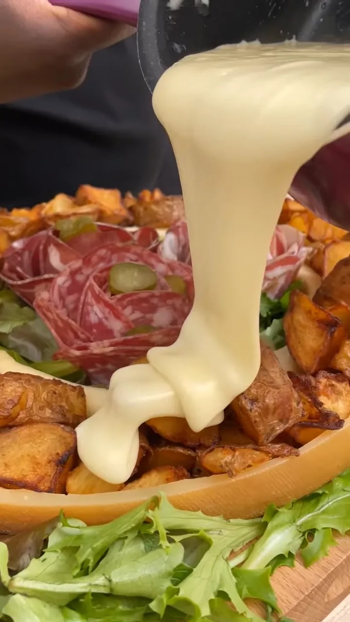 Fromage fondu versé sur des pommes de terre autour de rosaces de charcuterie