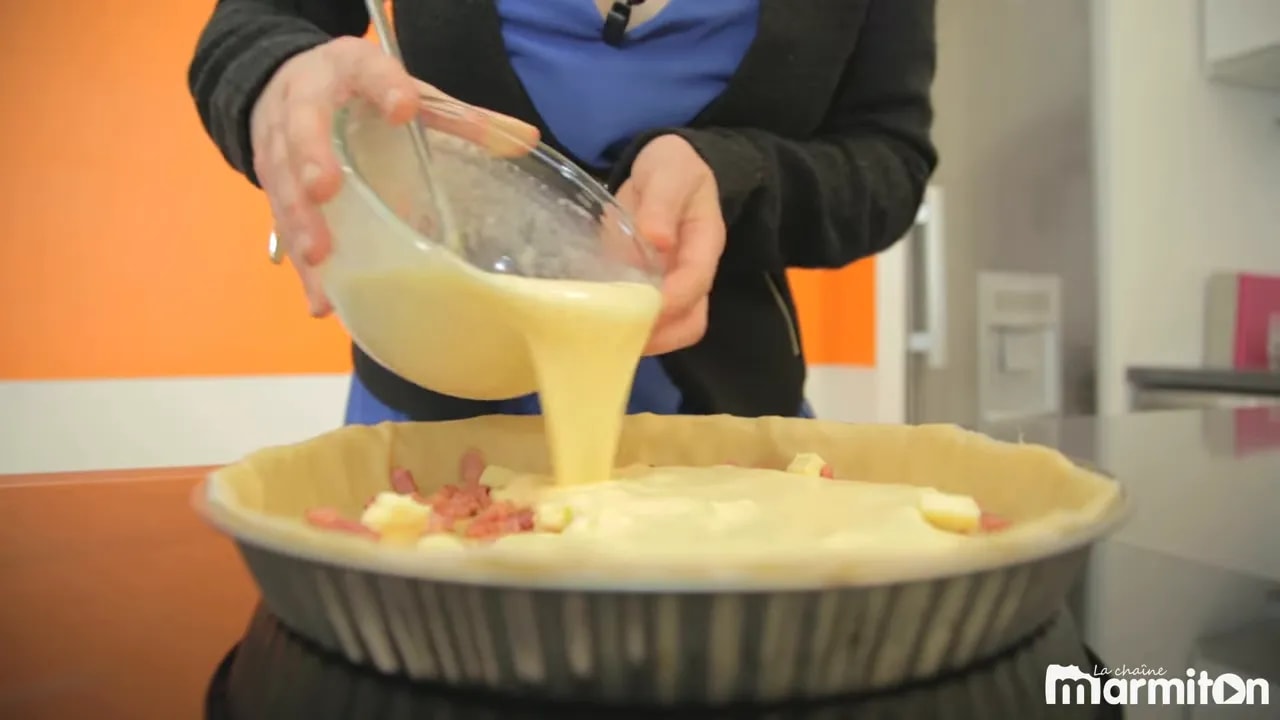 Appareil crémeux versé dans un moule à tarte garni de lardons et de dés de beurre